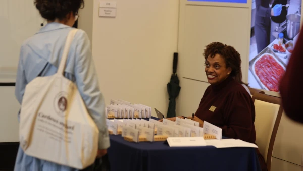 A staff member greets an attendee at the Emory University Senate meeting registration table with informational brochures