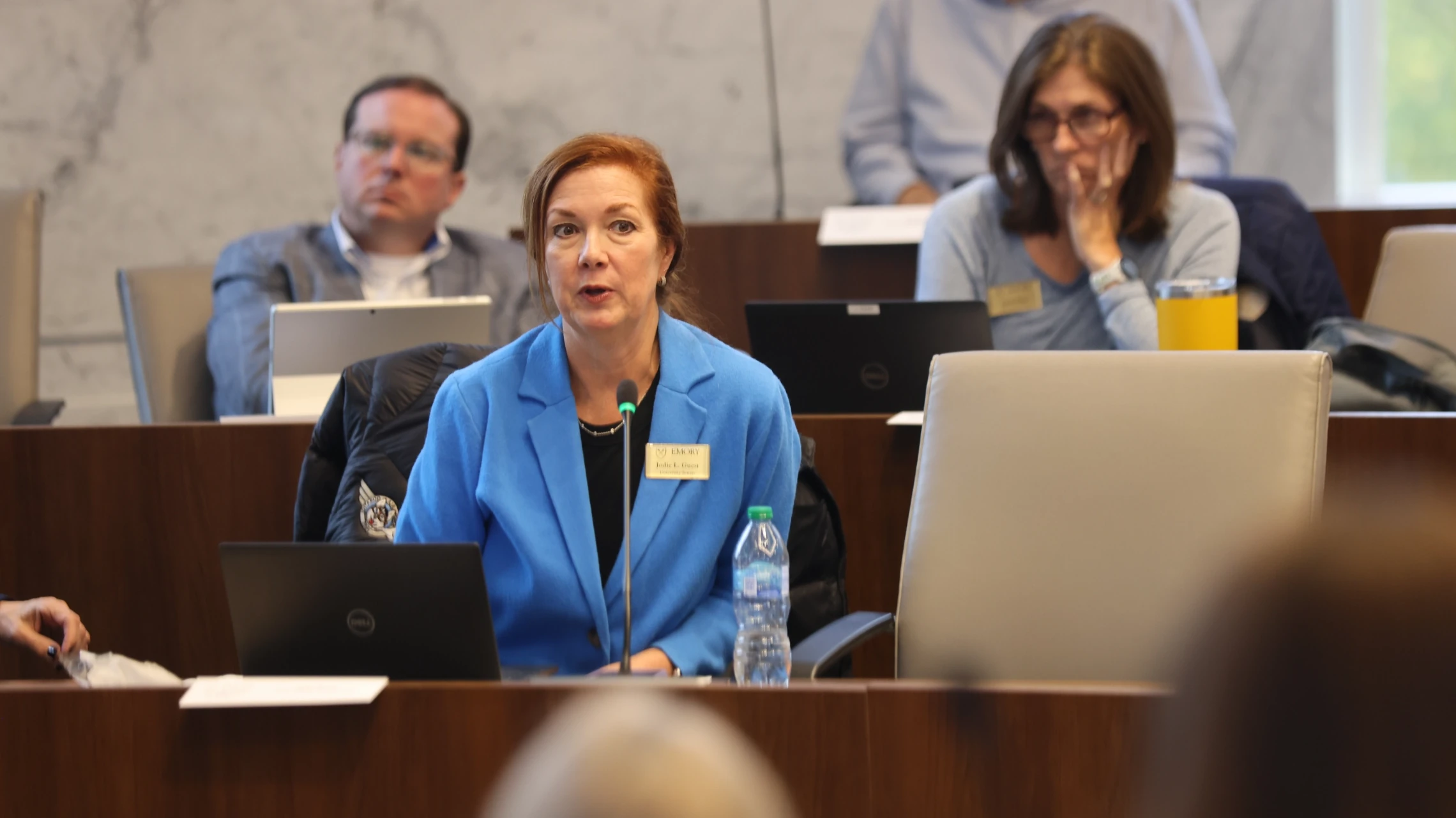Emory University Senate member in a blue blazer speaking into her microphone during the session