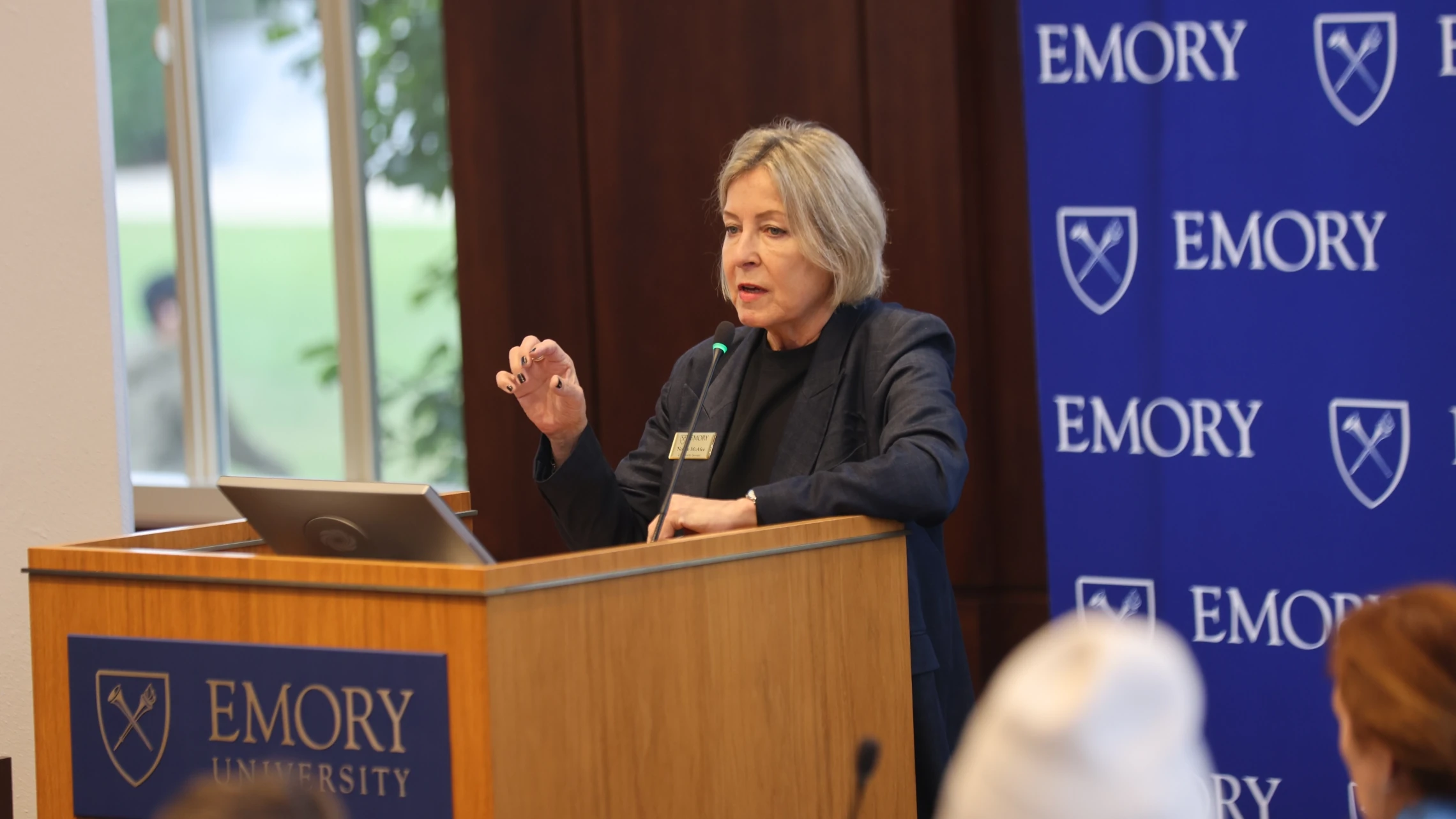 Speaker gesturing while speaking at the Emory University podium to Senate meeting attendees